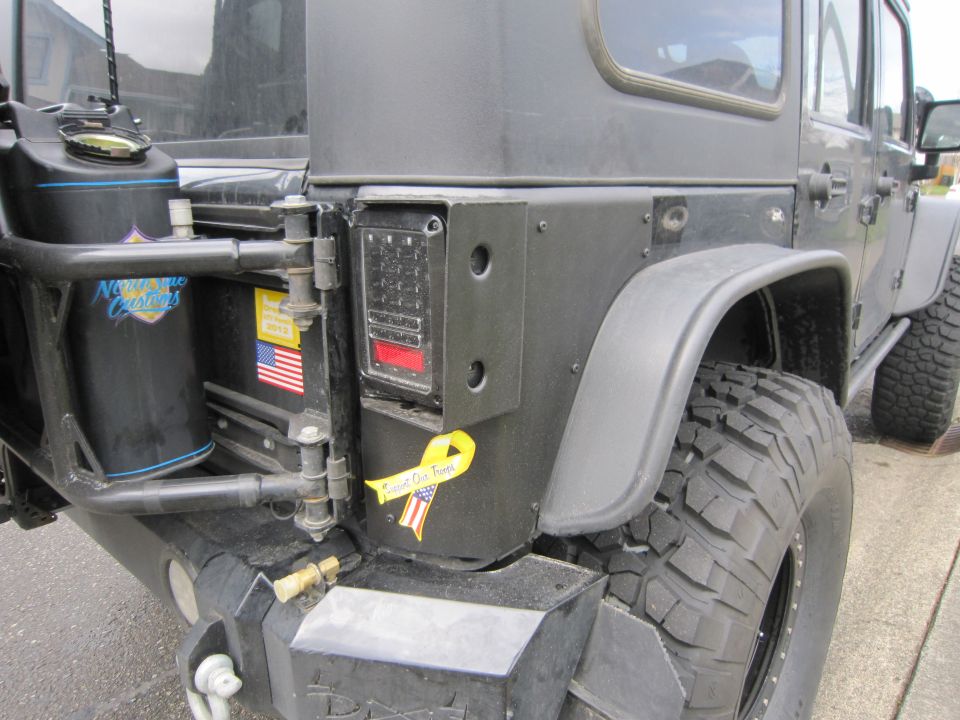 2008 Jeep Wrangler rear corner showing spare tire mount, jerry can, and aftermarket taillight. Yellow ribbon sticker is present