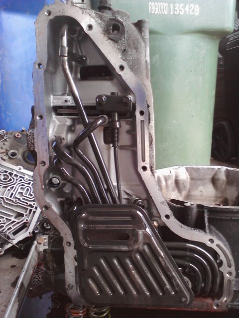 1993 Ford Taurus - Close-up of a transmission pan, showing the filter and internal tubing. Text is visible on a green container in the background.