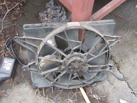 1972 Ford F-250 - A radiator fan assembly is shown lying on the ground next to a black bottle with readable text.