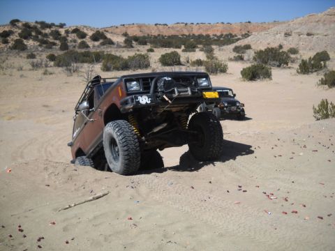 1986 Ford Bronco II - Two SUVs navigate sandy terrain with one vehicle partially stuck in the sand.