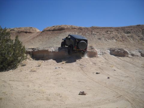 1986 Ford Bronco II - SUV navigates a challenging dirt trail with steep inclines and rocky terrain under a clear blue sky.