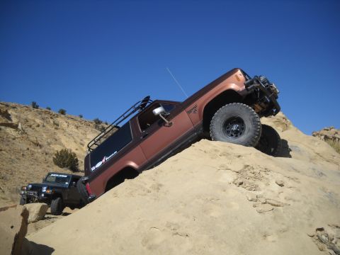 1986 Ford Bronco II - Two off-road vehicles navigate a steep, sandy incline under a clear blue sky.