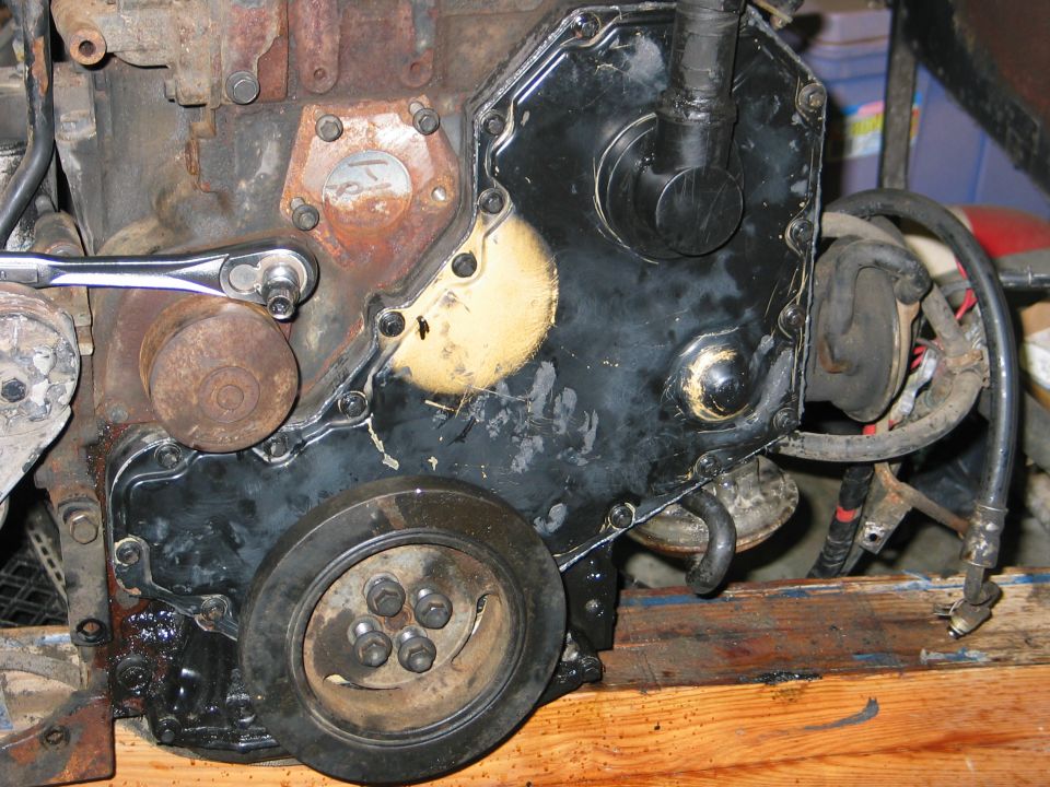 Engine timing cover with a socket wrench attached to a bolt, showing a pulley wheel and various hoses