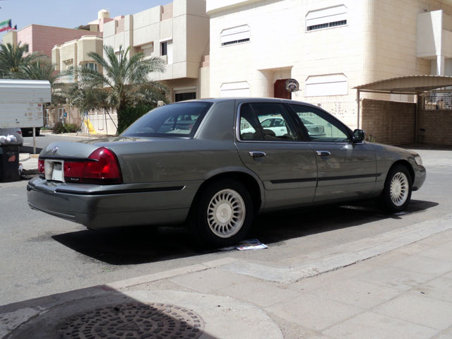 Rear three-quarter view of a gray-green Mercury Grand Marquis sedan parked at a curb