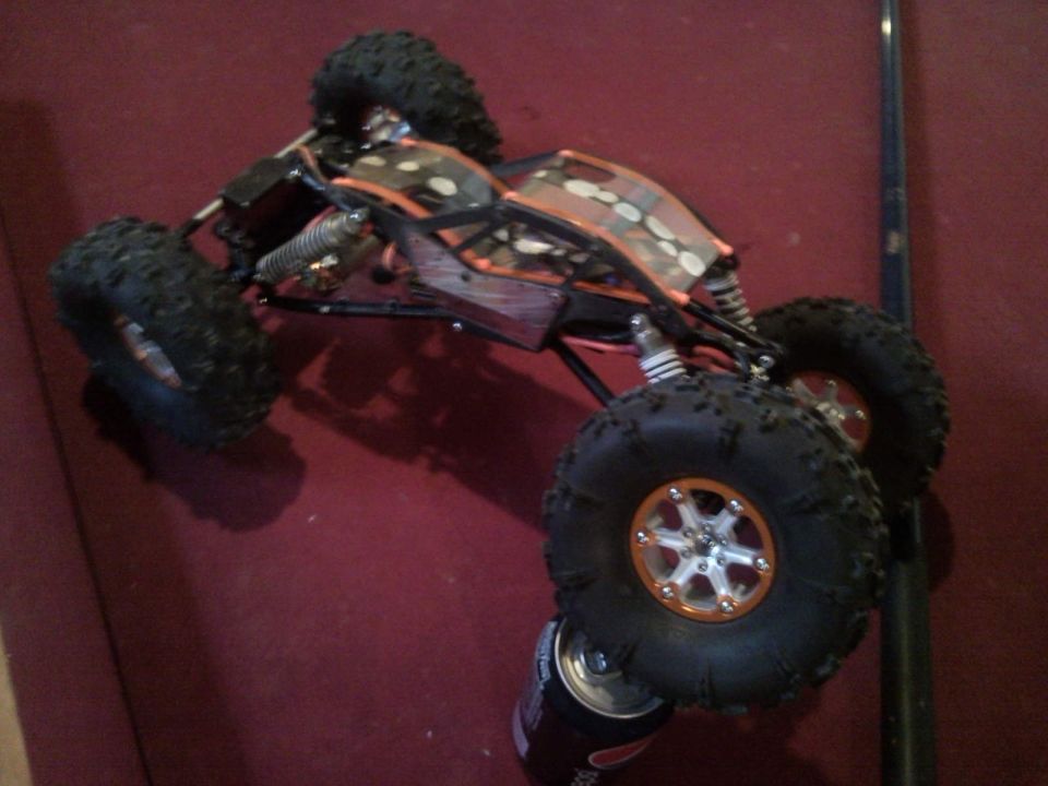 Remote control rock crawler with orange and black body, large tires, and silver rims