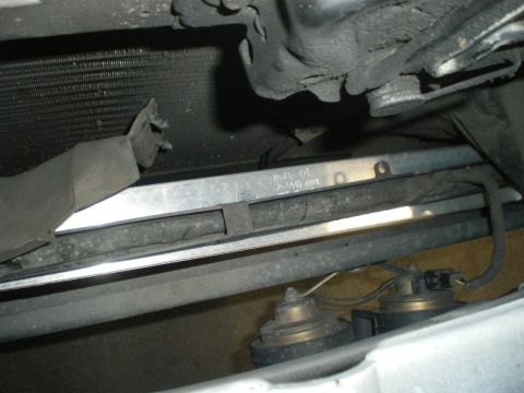 1998 Ford Crown Victoria - Detail of the front of a vehicle, showing the radiator, horns, and a metal support bar with a part number stamped on it.