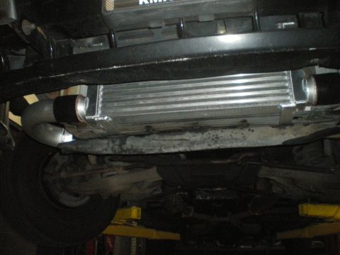 1998 Ford Crown Victoria - An aftermarket intercooler is installed on the underside of a vehicle, connected by silver piping.