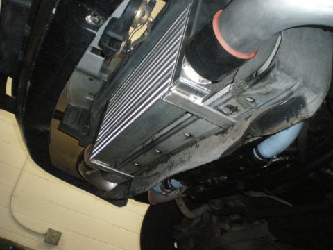 1998 Ford Crown Victoria - aluminum front-mount intercooler with a black silicone coupler installed below a vehicle, shot from underneath.