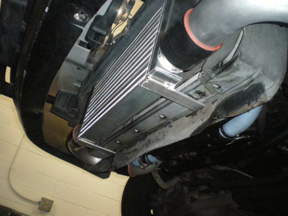 Front-mount intercooler with silicone coupler installed beneath a vehicle on white floor