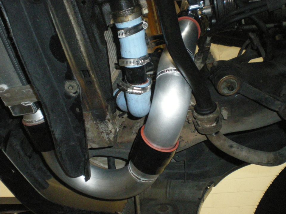 Underside view of blue silicone hoses, clamps, and an aluminum pipe near suspension