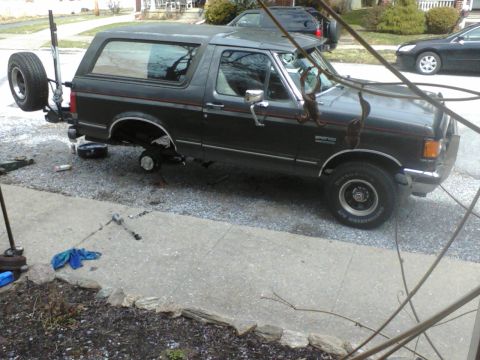 1988 Ford Bronco - A Ford Bronco is undergoing maintenance with its front wheel removed and spare tire attached to the rear.