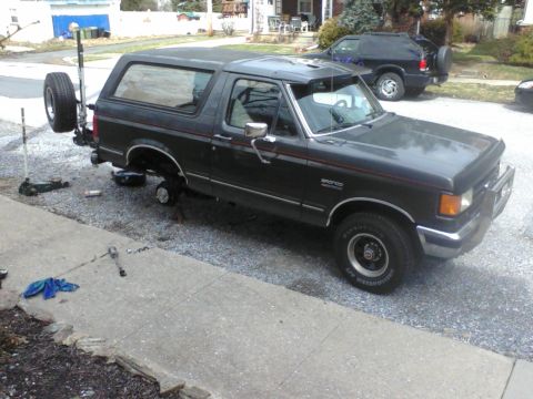 1988 Ford Bronco - A dark gray Ford Bronco is jacked up for maintenance, with its spare tire attached to the rear.