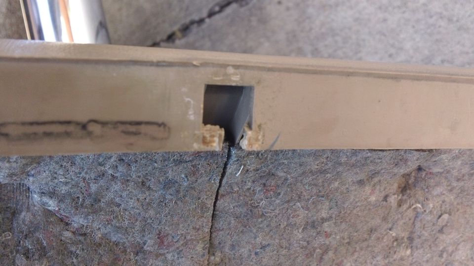 Cracked tan door panel edge with chipped mounting cutout on gray fiber backing