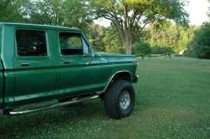 1995 Ford Bronco - A green four-door pickup truck is parked on a grassy lawn with trees in the distance.