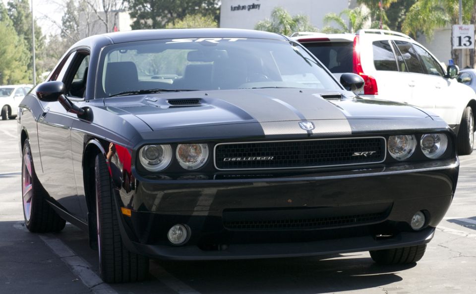 Black Dodge Challenger SRT with racing stripes, parked outside. White SUV behind it