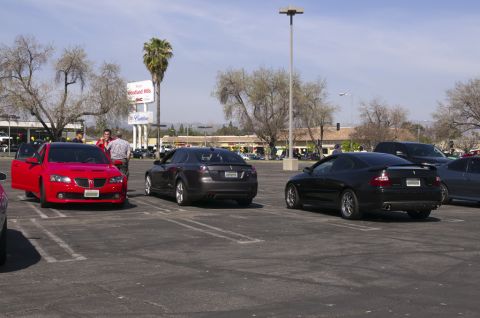 2006 Cadillac STS - A red Pontiac GTO is parked with its door ajar, alongside other vehicles in a parking lot.