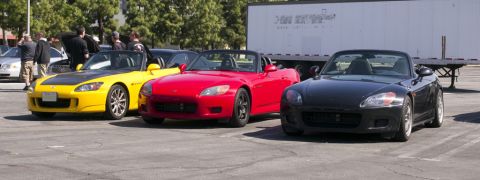 2006 Cadillac STS - Three Honda S2000 roadsters are lined up in a parking lot with a large trailer in the background.