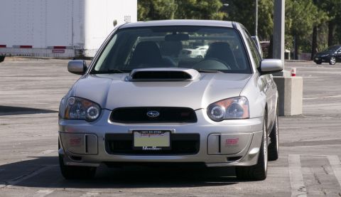 2006 Cadillac STS - A silver Subaru Impreza WRX STI is parked facing the camera, showing its distinctive hood scoop and front grille.