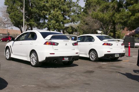 2006 Cadillac STS - Two white Mitsubishi Lancer Evolutions are shown from the rear, parked in a lot with trees and buildings in the background.