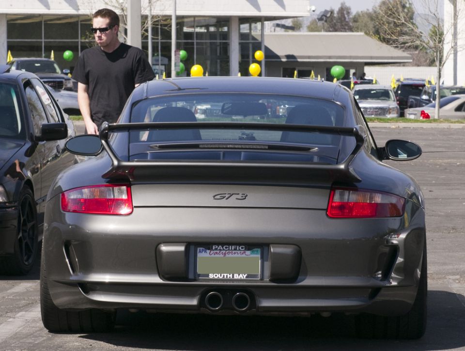 Rear view of a gray Porsche 911 GT3 with a spoiler and dual exhaust. A man stands beside it