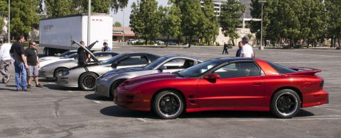 2006 Cadillac STS - Several sports cars are parked in a lot with people gathered around them, including a red Pontiac Firebird.