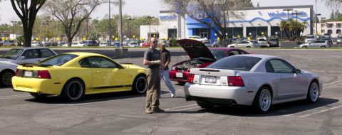2006 Cadillac STS - Two Ford Mustang Cobras are parked in a lot with two men standing nearby.