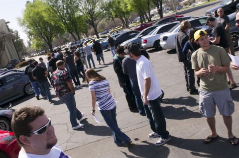 2006 Cadillac STS - A group of people stand around several cars parked in a lot on a sunny day.