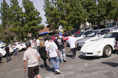 2006 Cadillac STS - A group of people gather around a white sports car parked in a lot with other vehicles.