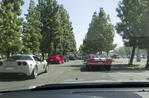 2006 Cadillac STS - A line of cars, including a Corvette and a classic muscle car, drive down a street lined with trees.