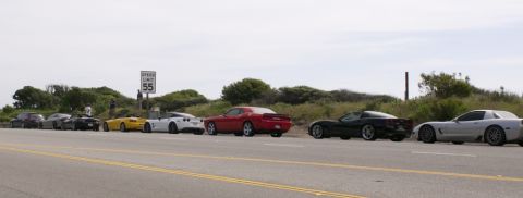 2006 Cadillac STS - A group of sports cars, including Corvettes and a Challenger, are parked along a roadside with a speed limit sign.