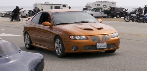 2006 Cadillac STS - Orange Pontiac GTO with distinctive hood scoops and grille, seen on a street with other vehicles.