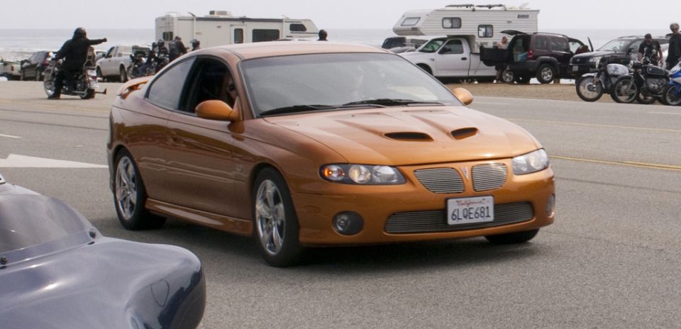 Orange Pontiac GTO with California plates 6LOE681 parked on a street with other vehicles and motorcycles