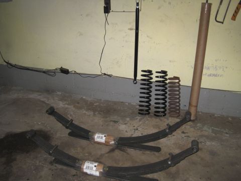 1979 Ford Bronco - Leaf springs and coil springs are laid out on the floor, along with a shock absorber and a cardboard tube.
