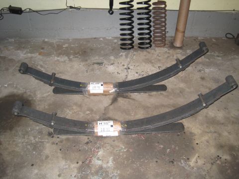 1979 Ford Bronco - Suspension parts, including leaf springs and coil springs, are laid out on a garage floor.