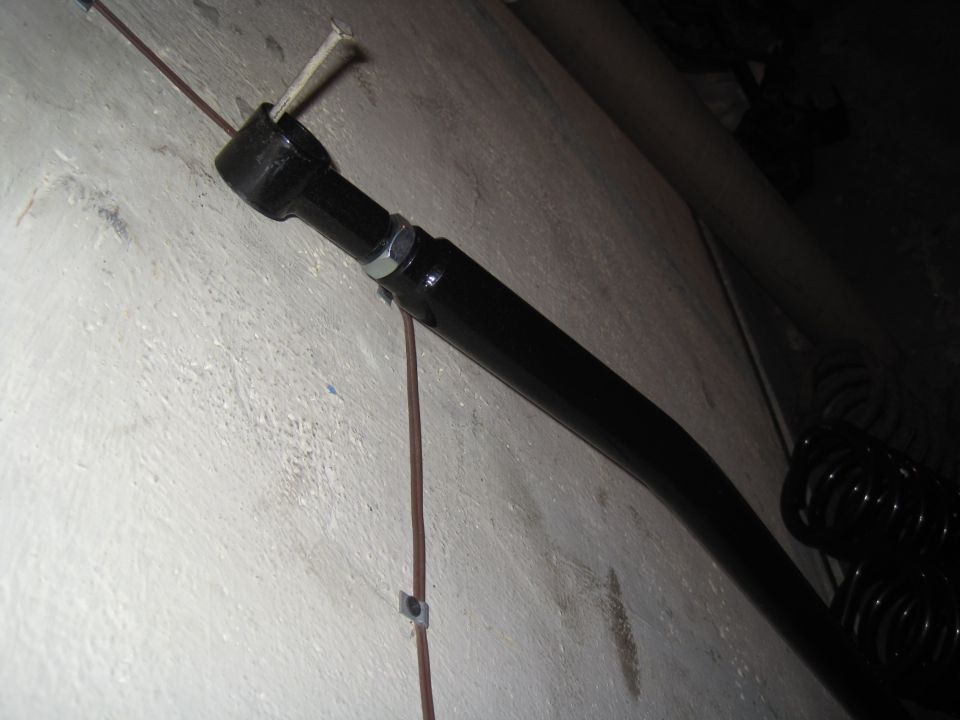 Black suspension arm with a bolt and nut, attached to a white wall