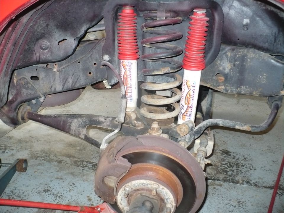 Front suspension with red-booted shocks and brake rotor. SuperMotors.net logo visible