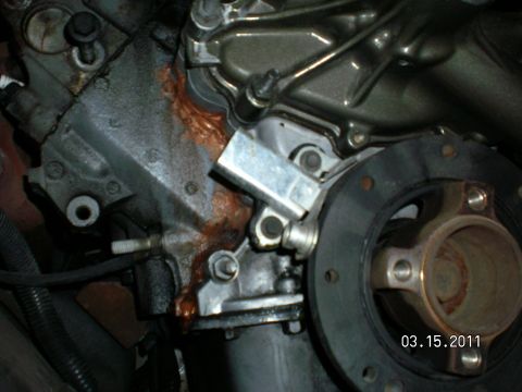 1996 Ford Bronco - Front of an engine showing the timing cover, hub flange and rust-colored coolant staining from a leak.