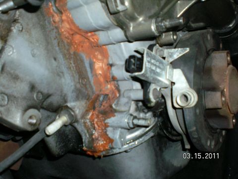 1996 Ford Bronco - Close-up of the front of an engine during assembly, showing a thick orange RTV silicone bead squeezed out along the timing-cover-to-block s…