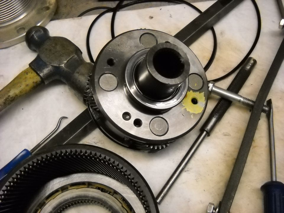 Transmission gears and a hammer on a workbench. Tools like a file and screwdrivers are also visible