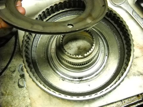1993 Ford C-150 (Centurion Conversions) - A mechanic's hand holds a metal ring over a complex gear assembly, likely part of a transmission rebuild.