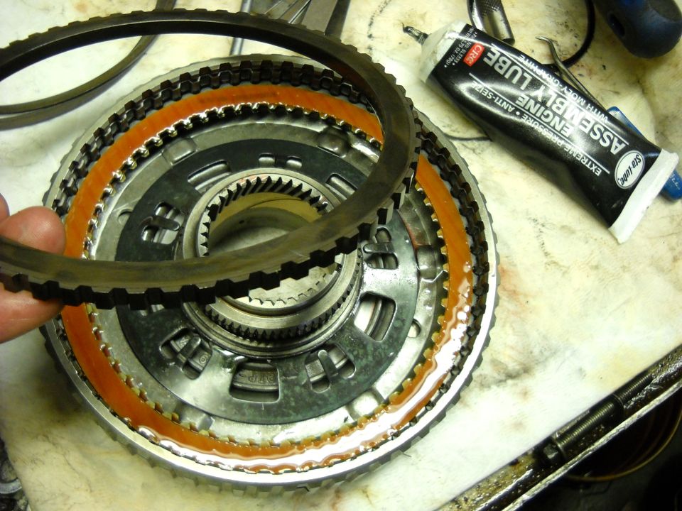 Close-up of an automatic transmission clutch pack with a hand holding a friction ring. Tube of assembly lube nearby