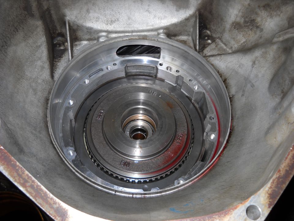 Transmission torque converter housing with internal components visible. Metal casing shows some wear and staining