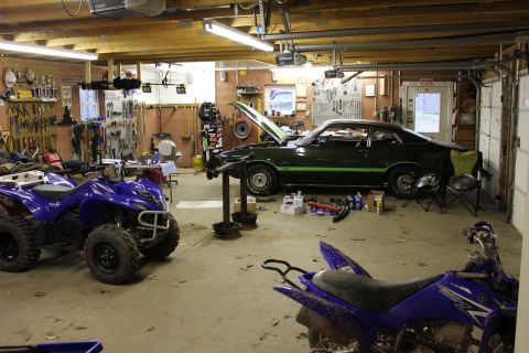 1985 Ford Bronco - A green muscle car with racing stripes is parked in a garage next to ATVs.