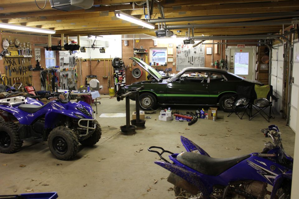 Green muscle car with black hood and green stripes, hood up, parked in a garage with ATVs