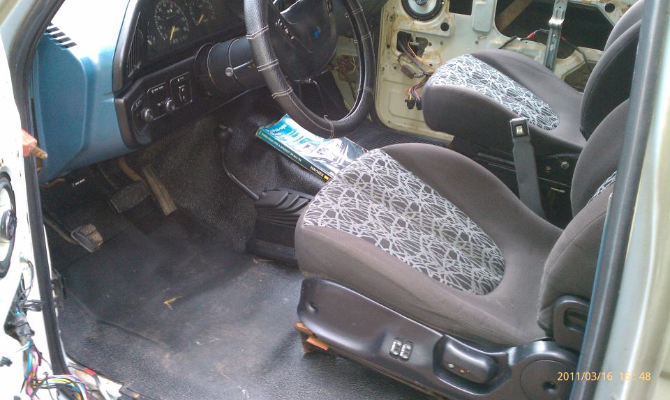 Interior of a vehicle, showing seats, dashboard, steering wheel, and floor pedals. Door panel is removed