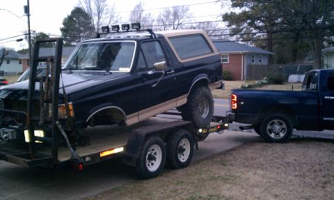 1990 Ford Bronco - Ford Bronco being transported on a trailer, towed by a pickup truck.