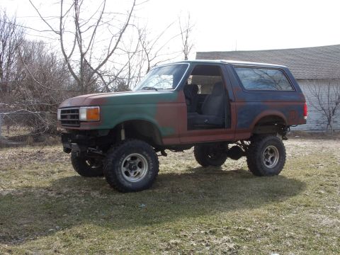 1988 Ford Bronco - This lifted 1987 Ford Bronco features a unique camouflage paint scheme and an open driver's door, revealing the interior.
