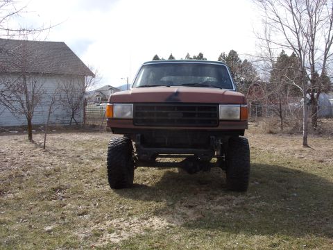 1988 Ford Bronco - This lifted pickup truck is parked in a yard with a barn and trees in the background.
