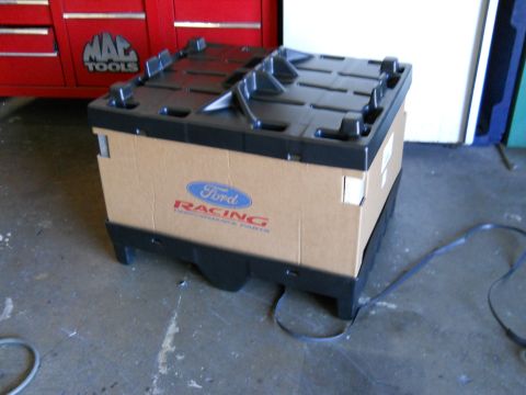 2003 Ford Crown Victoria - A cardboard box labeled "Ford Racing Performance Parts" sits on a black plastic pallet in a garage.
