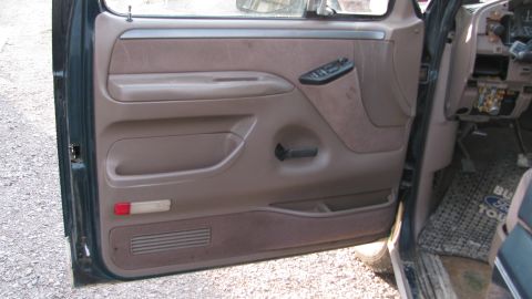 1992 Ford Bronco - The interior door panel of a 1992 Ford Bronco shows brown fabric and plastic components, including the window controls and door handle.